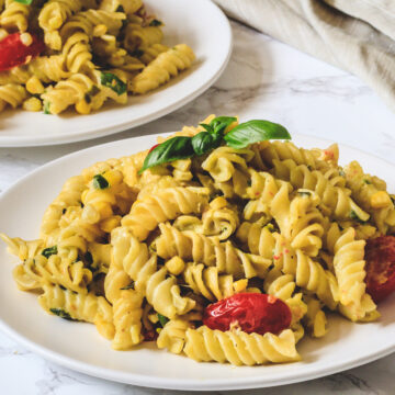 Corn pasta garnish with basil leaves in a white plate with another plate in the back with napkin