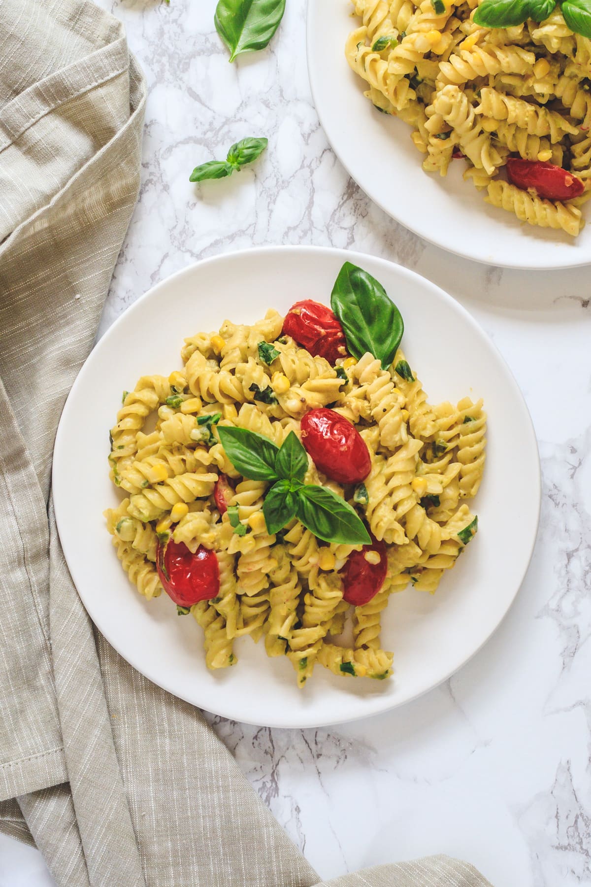 Corn pasta served in two plates garnished with basil leaves and napkin on side