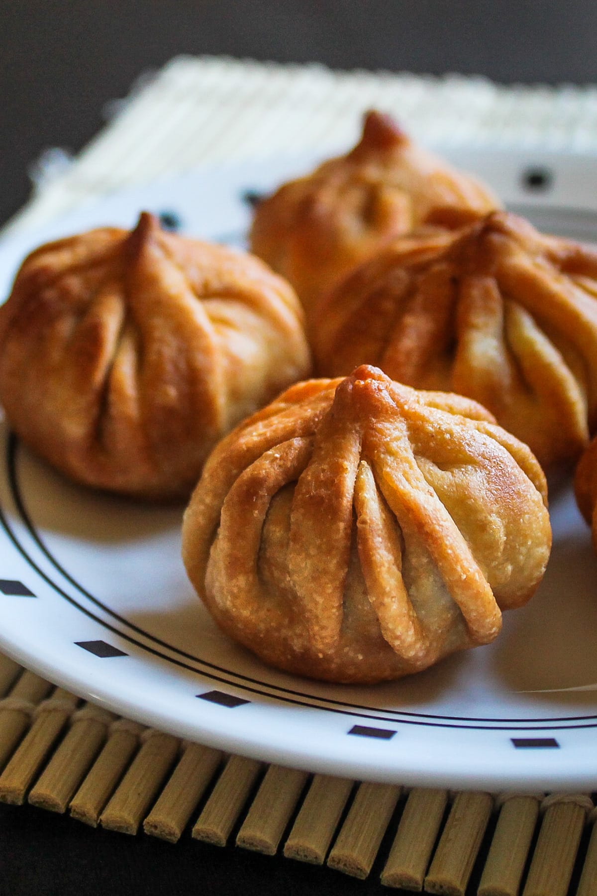 Close up of fried modak on a plate with bamboo mat underneath