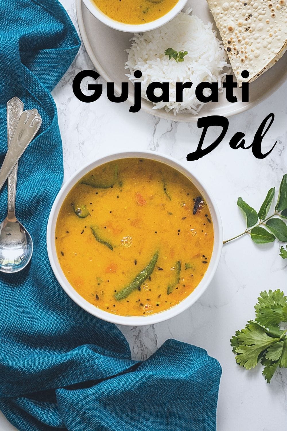 Gujarati dal in a bowl with rice and papad on side with napkin, spoons and cilantro leaves laid around the bowl