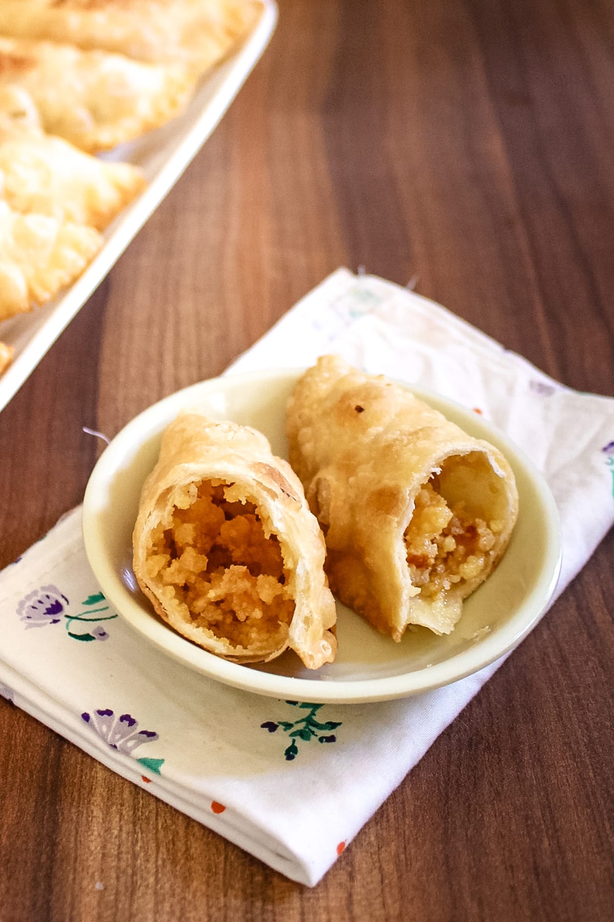 Gujia cut into half to show inside stuffing in a small plate with napkin under the plate.