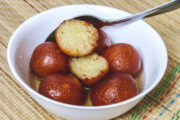 Gulab jamun in a bowl with one jamun cut open with a spoon