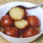 Gulab jamun in a bowl with one jamun cut open with a spoon