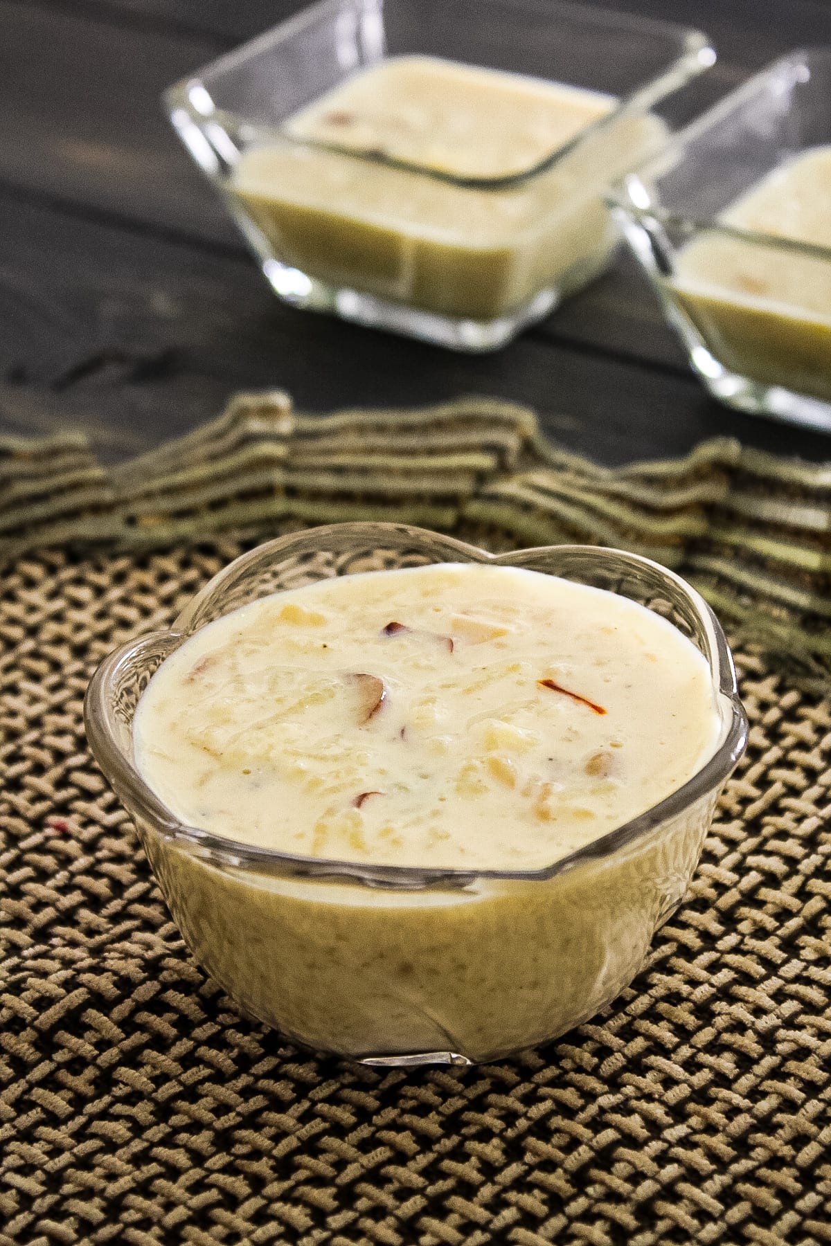 kheer in a bowl with decorative napkin underneath and 2 bowls of kheer in the back