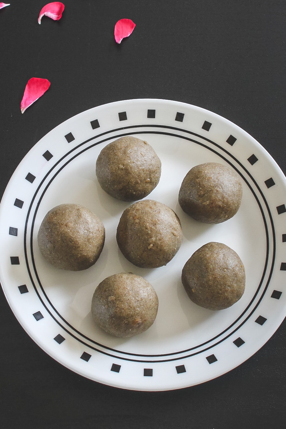 6 bajra ladoo on a plate with rose petals on side as a garnish