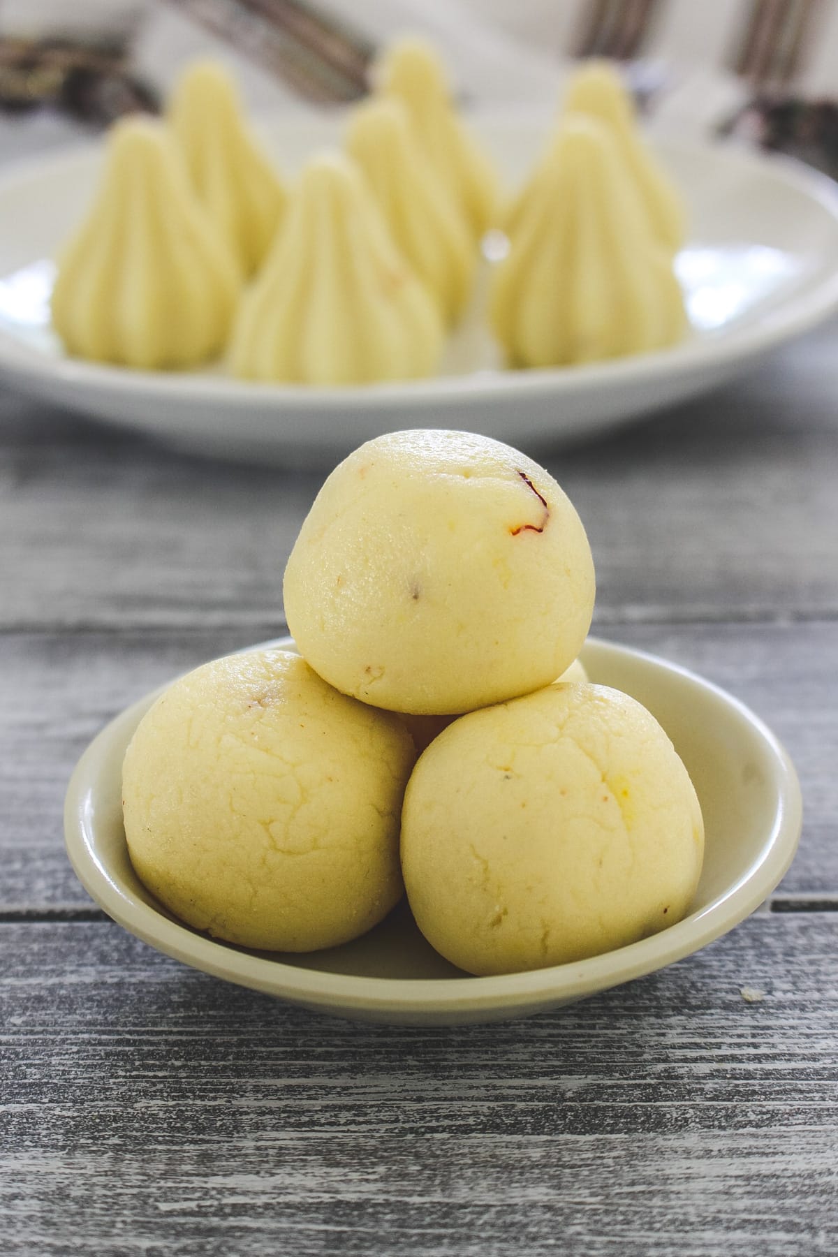 stack of 3 Malai ladoo in a small plate with malai modak on the back side