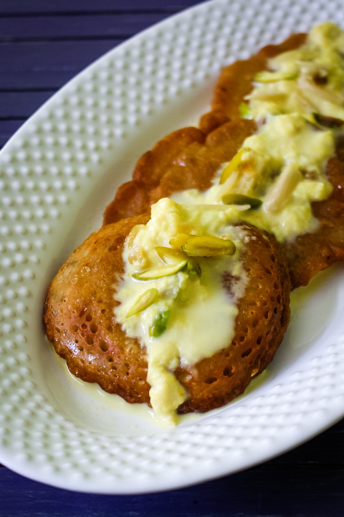 3 malpua in a plate and topped with rabdi and garnish with nuts