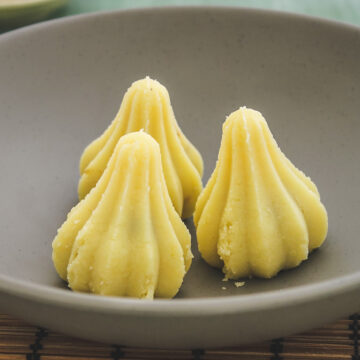 three stuffed mawa modak in a plate with wooden mat underneath