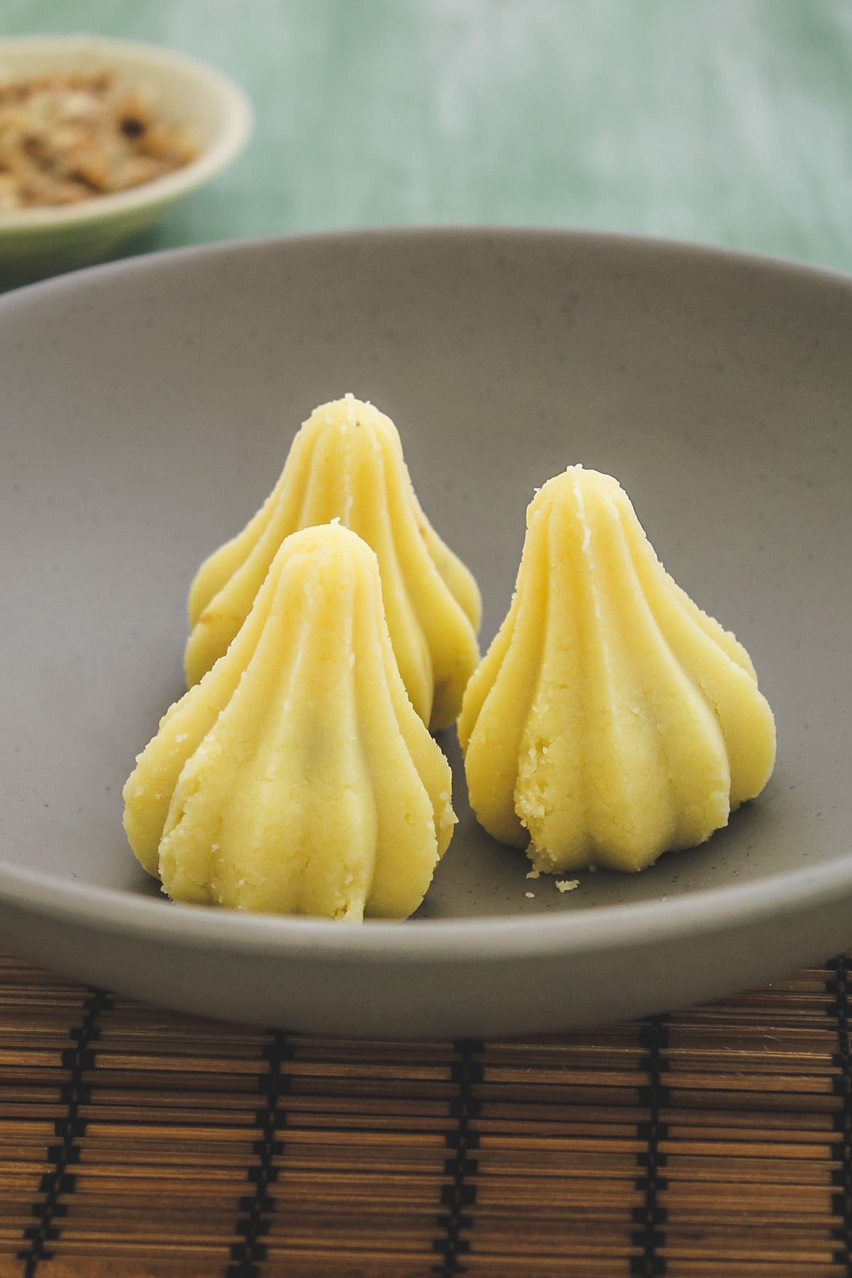 three stuffed mawa modak in a plate with wooden mat underneath