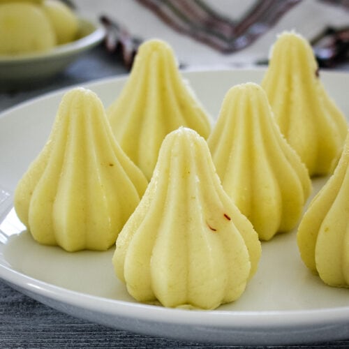 5 malai modak arranged on a plate with ladoo on the back side