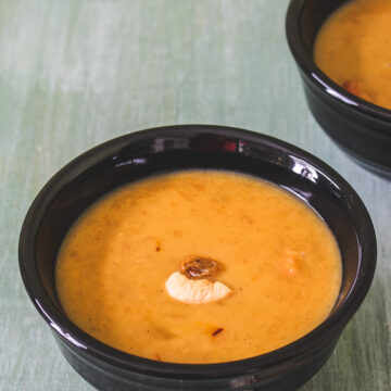 Paruppu payasam in a black bowl with garnish of fried cashew and raisin