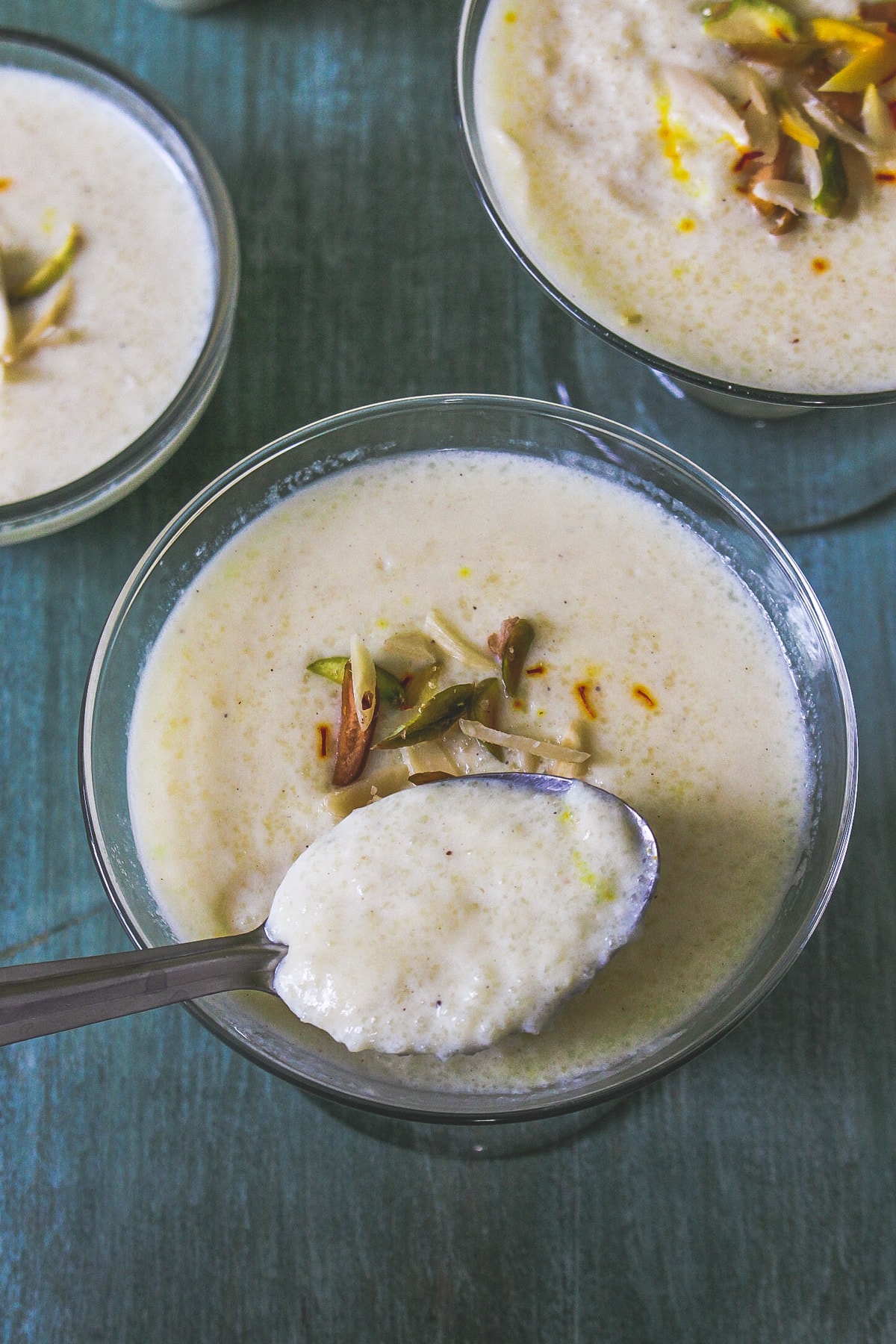 phirni served in 3 individual bowls and a spoonful of taken from one bowl, ready to eat