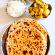 two puran poli in a steel plate with rice, bhaji and amti in steel bowl on side.