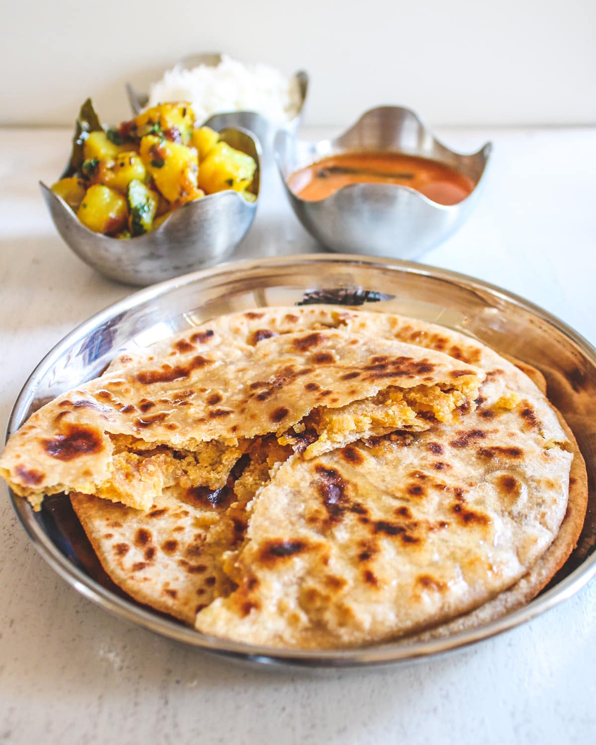 Image of puran poli cut into half to show inside stuffing. Bowls of bhaji, amti and rice on back