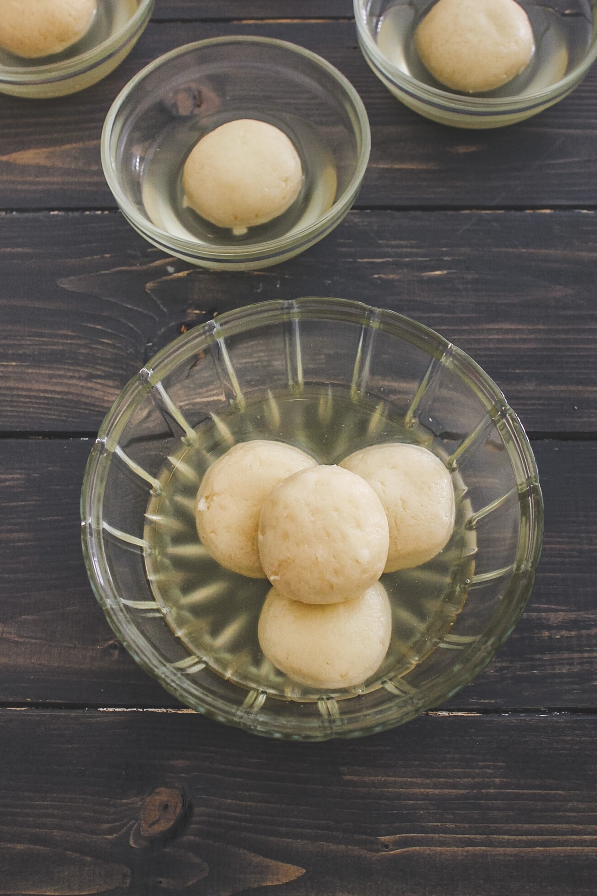 4 rasgullas in a bowl with 3 bowls with single ragulla in the back