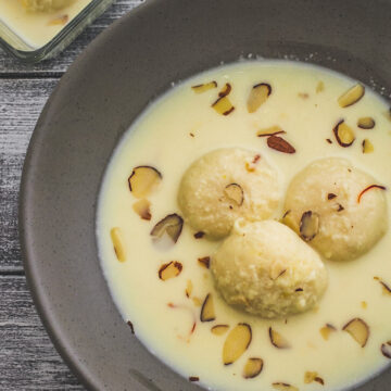 3 pieces of rasmalai in a gray bowl with garnish of almonds with one rasmalai in a small bowl in the back