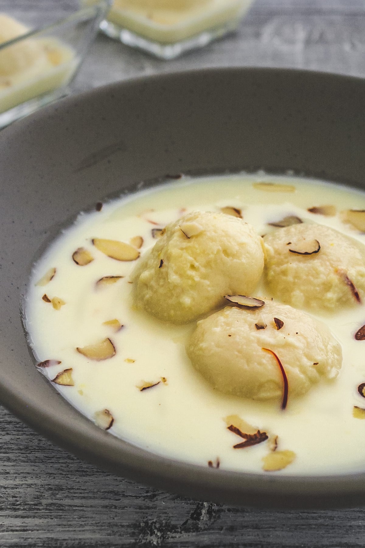 Close up of rasmalai garnished with slivered almonds in gray bowl