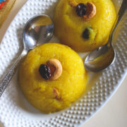 two scoops of rava kesari with garnish of cashew and raisin with 2 spoons in an oval plate