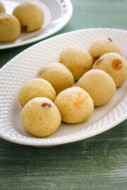 7 rava laddu in an oval plate with few more ladoos in the back in another plate