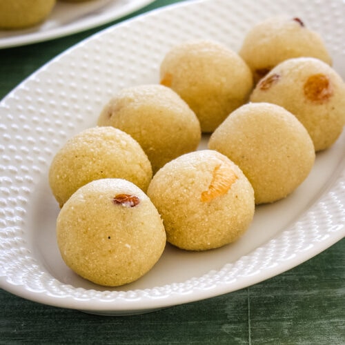 7 rava laddu in an oval plate with few more ladoos in the back in another plate