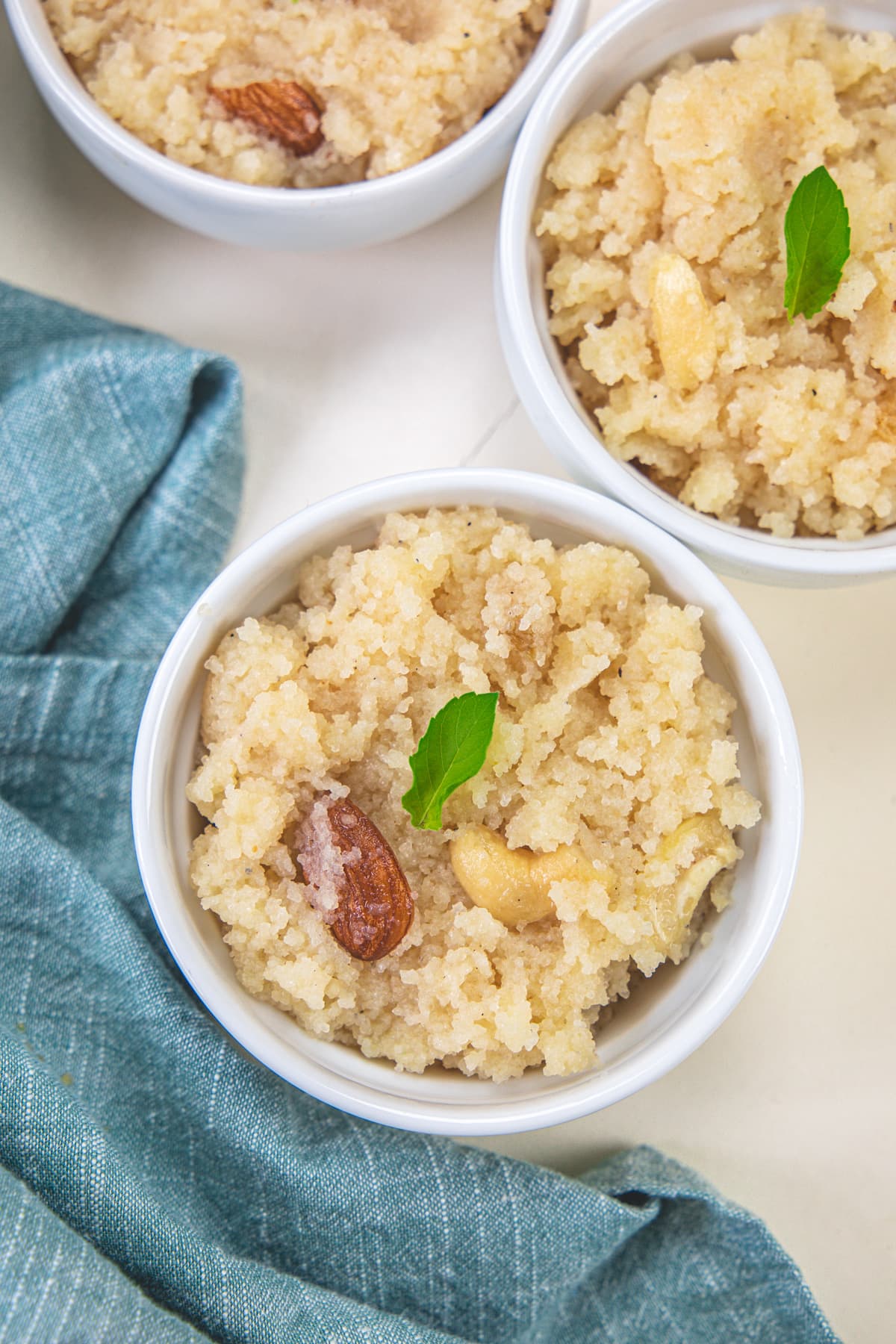 Rava sheera served in white bowls and garnished with tulsi leaves.