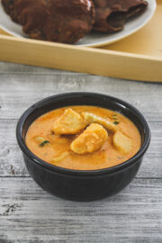 dahi arbi in a black bowl served with puri in the background