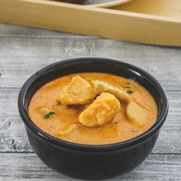 dahi arbi in a black bowl served with puri in the background