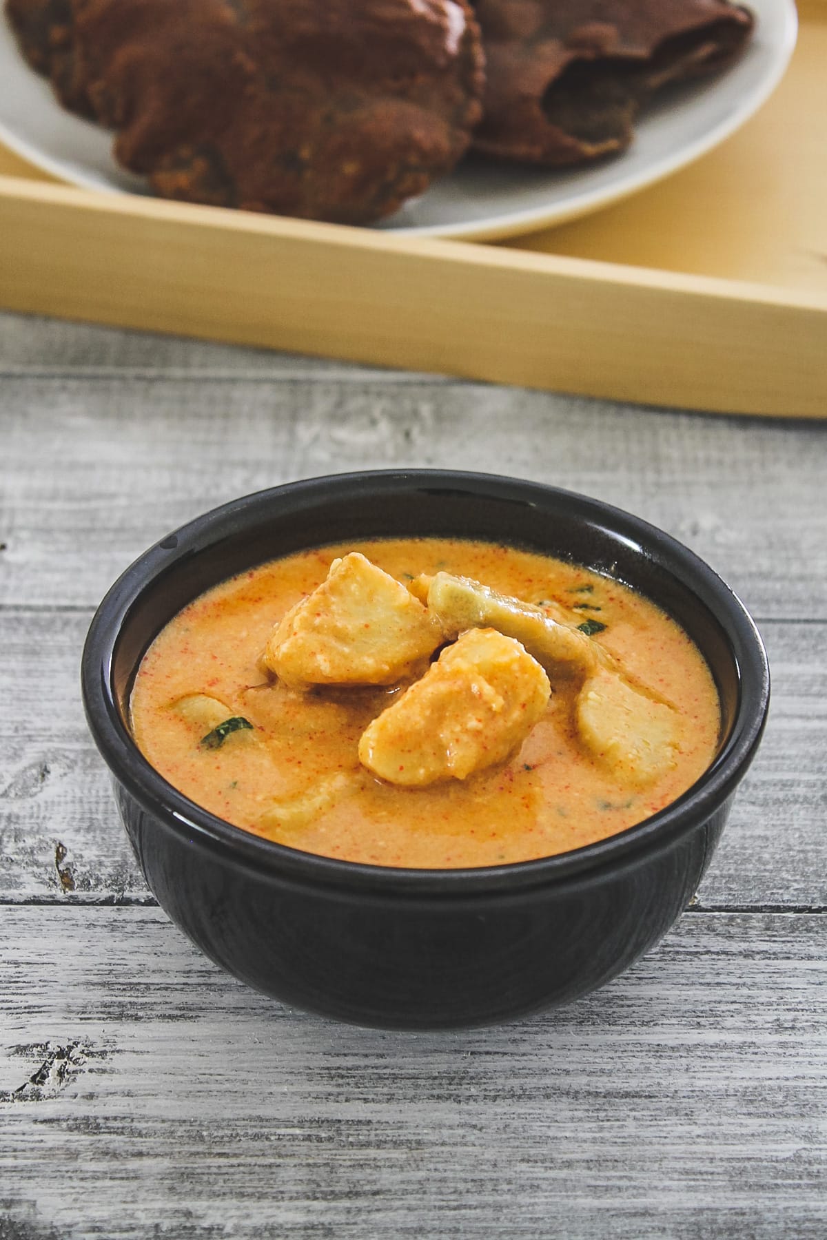 dahi arbi in a black bowl served with puri in the background