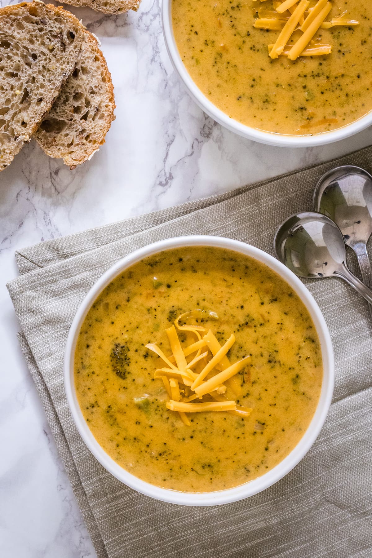 broccoli cheddar soup in a bowl with spoons & bread on side and napkin underneath.