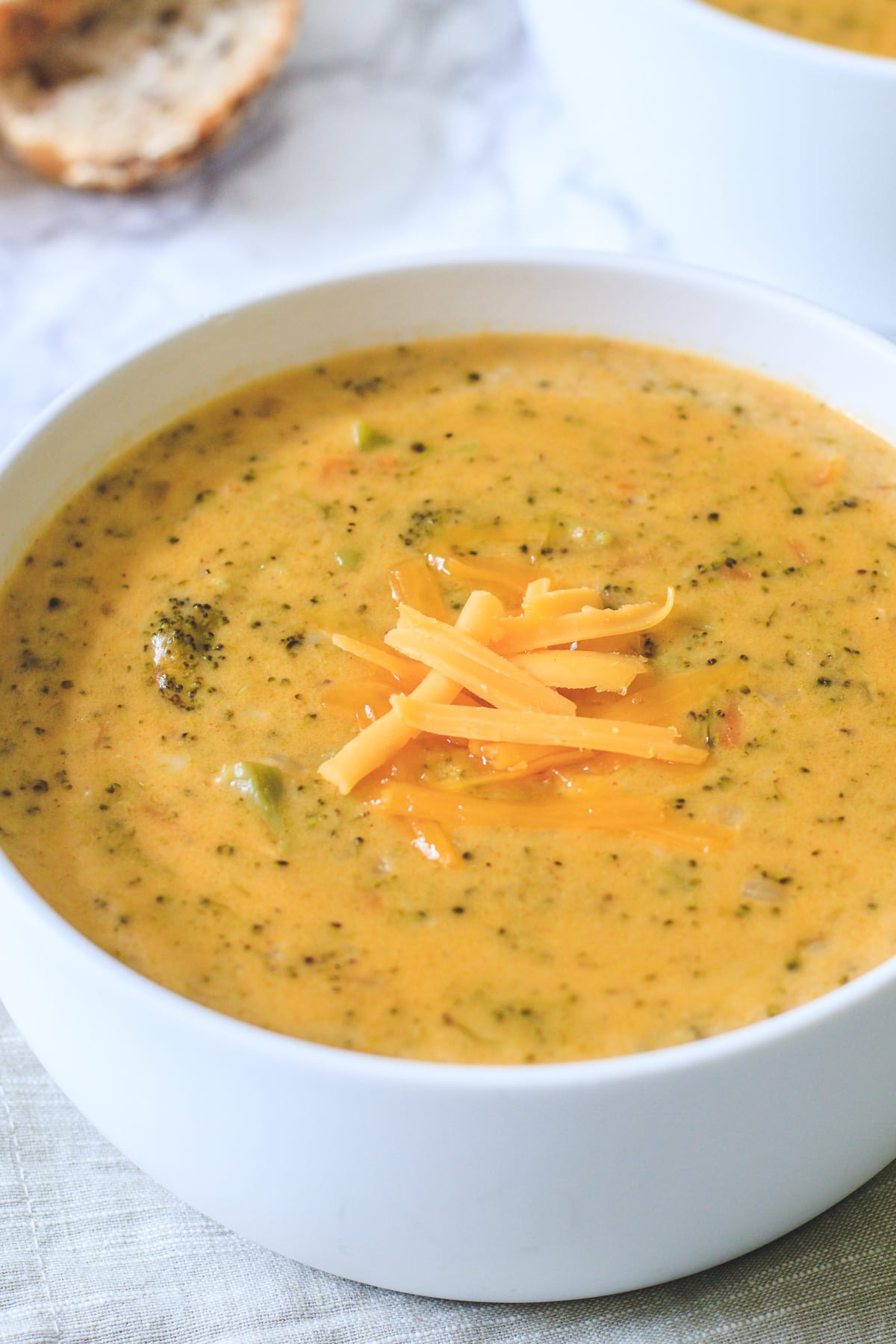 Close up of broccoli cheddar soup in a white bowl with cheese garnish