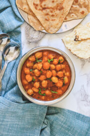 Top view of jain chole served in handi with paratha and papad with napkin and spoons on side.