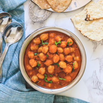 Top view of jain chole served in handi with paratha and papad with napkin and spoons on side.