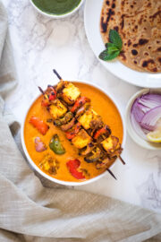 paneer tikka masala gravy with 2 skewers on the bowl, served with paratha, onions, chutney, lemon wedge