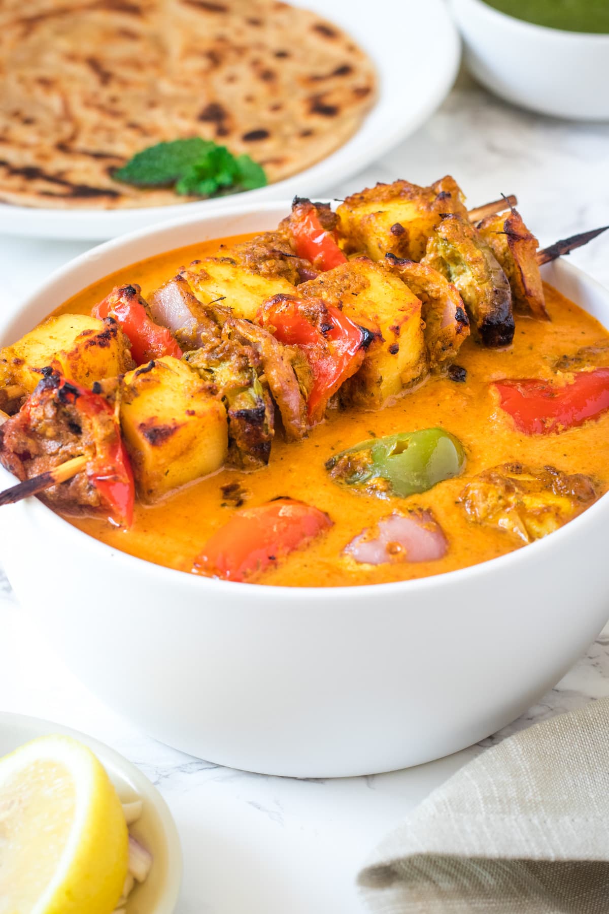 Close up of paneer tikka masala in a bowl with 2 tikka skewers rested on the bowl