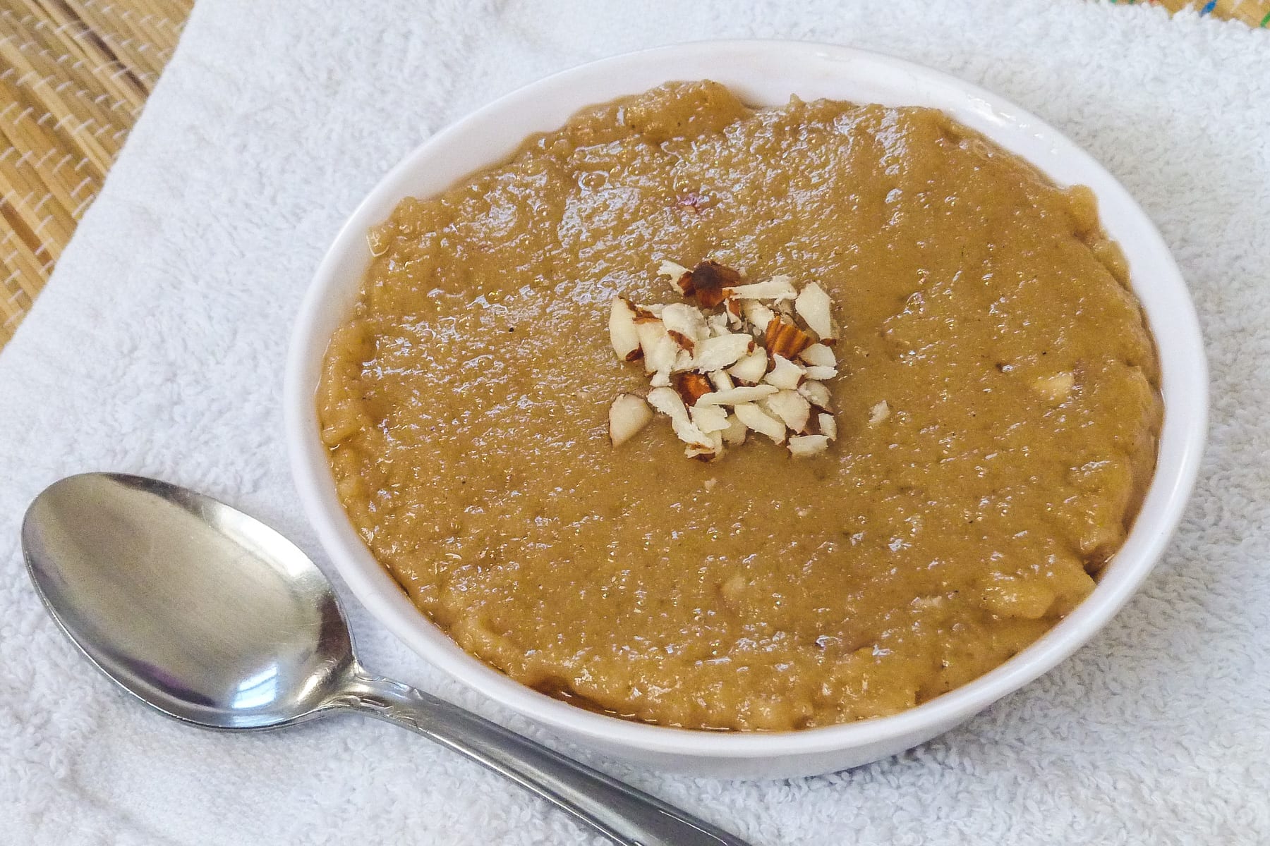 rajgira sheera in a bowl with garnish of chopped almonds with spoon on the side