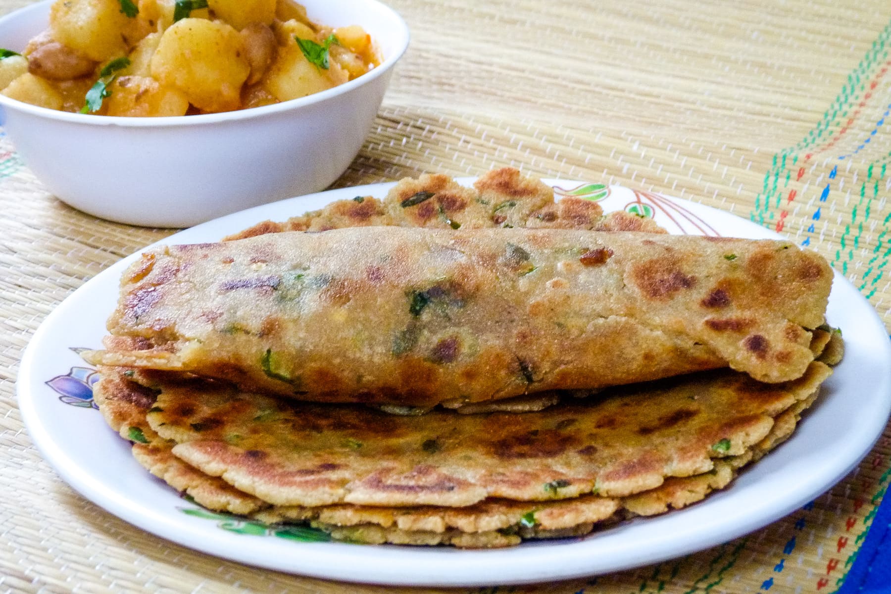 Rolled rajgira paratha on top of stack of paratha in a plate with aloo sabzi in back