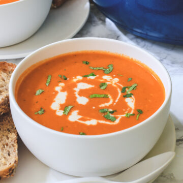 Roasted red pepper gouda soup in a bowl with side of bread.