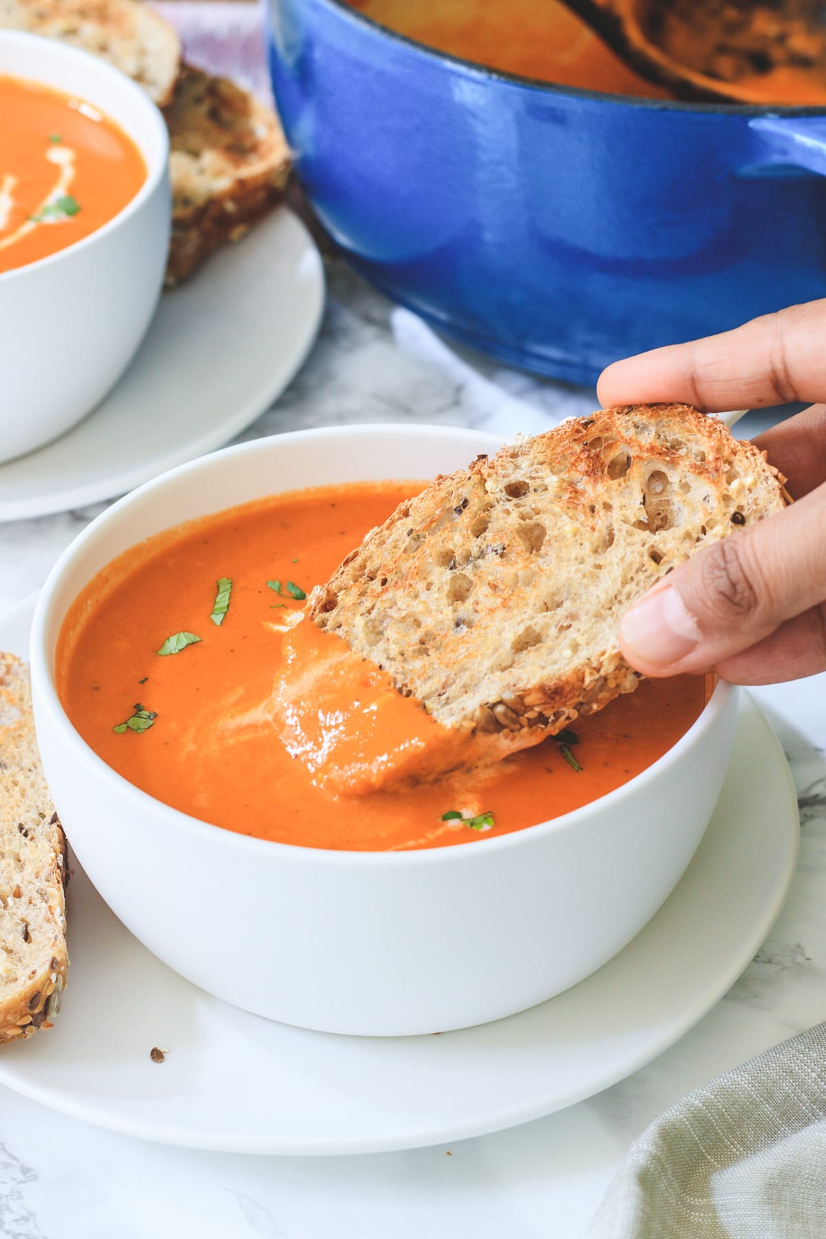 A bread dunked into the roasted red pepper soup ready to eat.