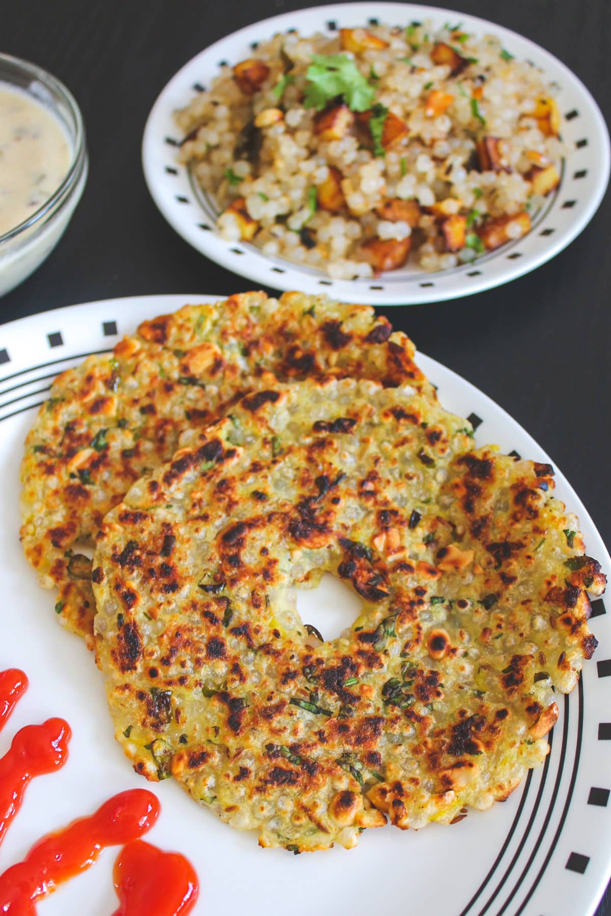 sabudana thalipeeth in a plate with ketchup on side and khichdi served in the back