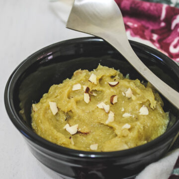 sweet potato halwa in a black bowl with a steel spoon rested on the bowl.