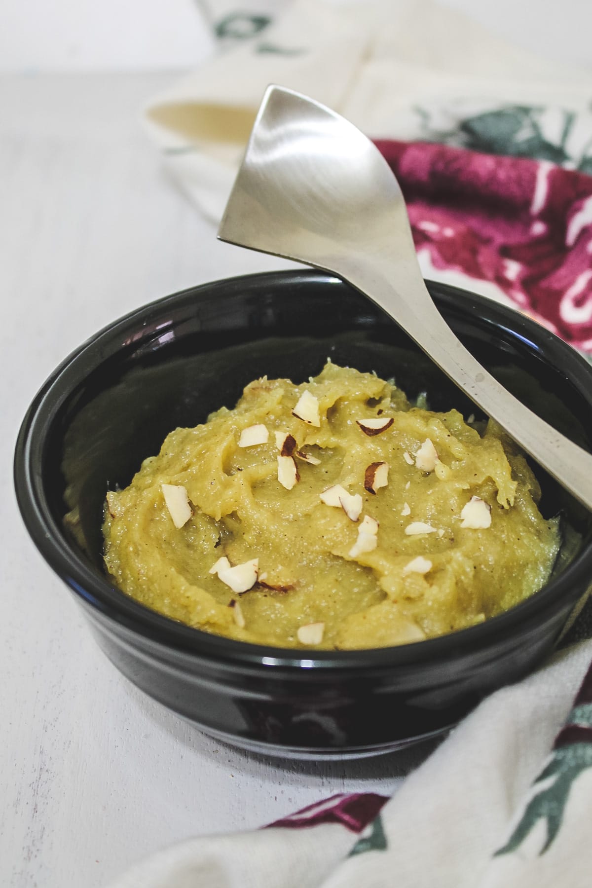 sweet potato halwa in a black bowl with a steel spoon rested on the bowl.