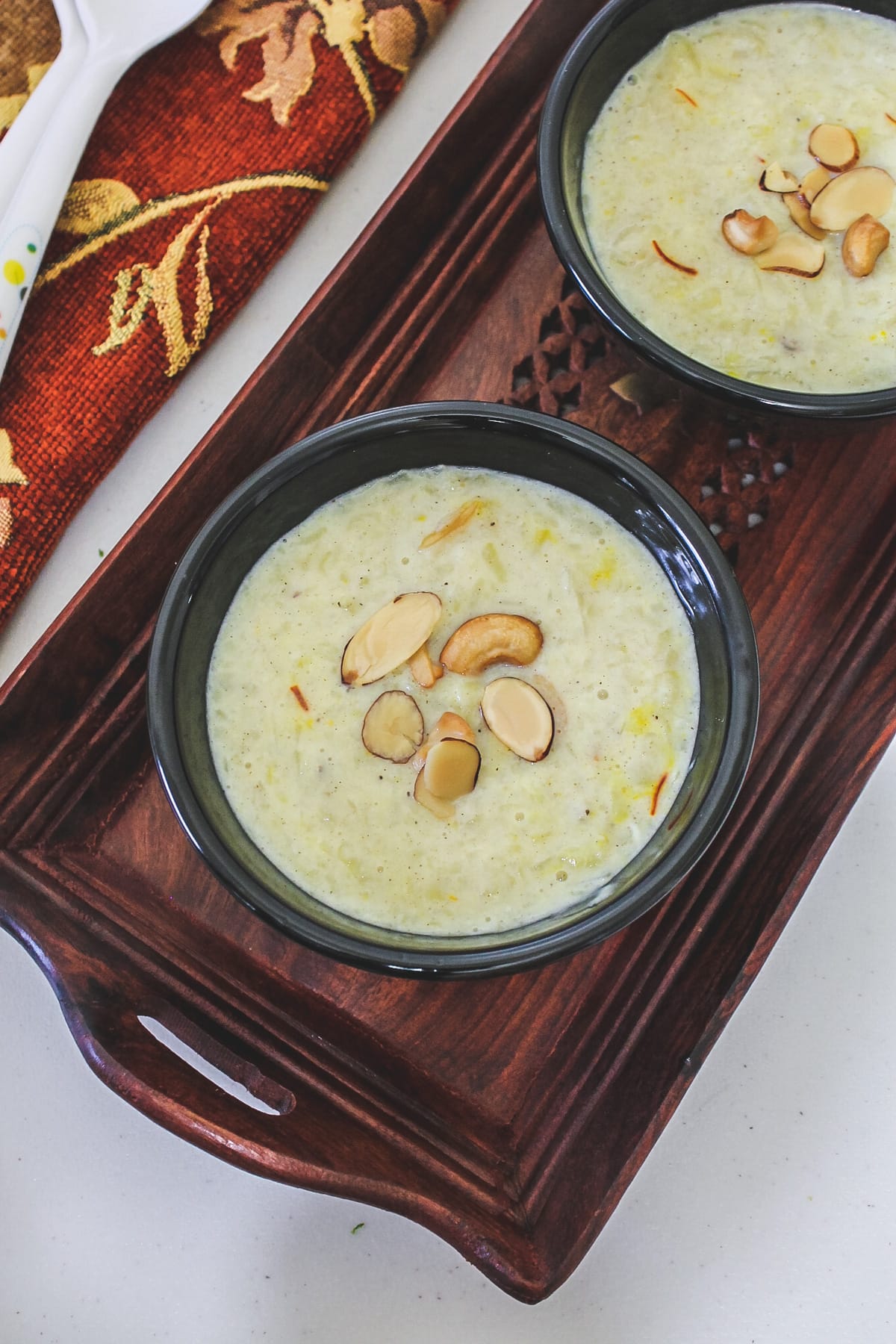 2 bowls of sweet potato kheer garnished with nuts in a wooden tray