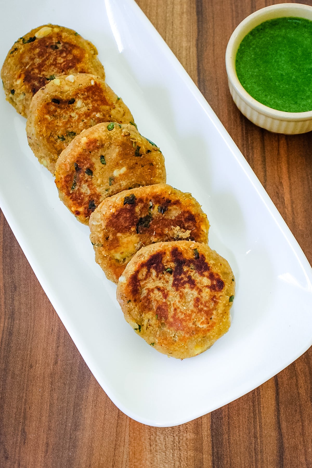 5 sweet potato tikki arranged in a plate with cilantro chutney on side