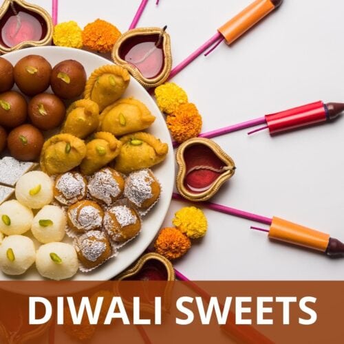 Assortment of Indian sweets in a plate with diya and firecrackers around the plate.