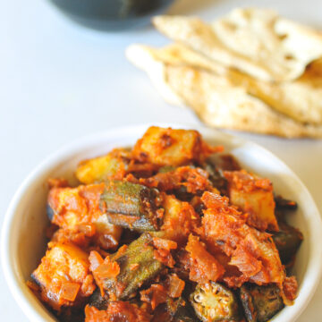 aloo bhindi served in a bowl with papad and stacked bowls in the back.