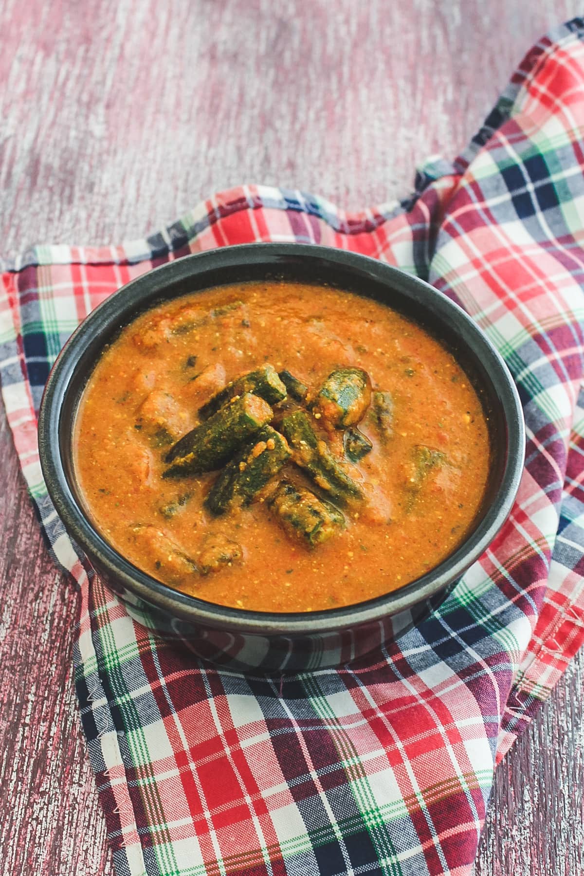 Okra curry in black with with checkerboard napkin underneath.