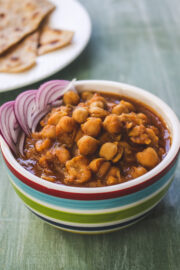 Chana masala in a bowl with garnish of sliced onions, paratha in the back.
