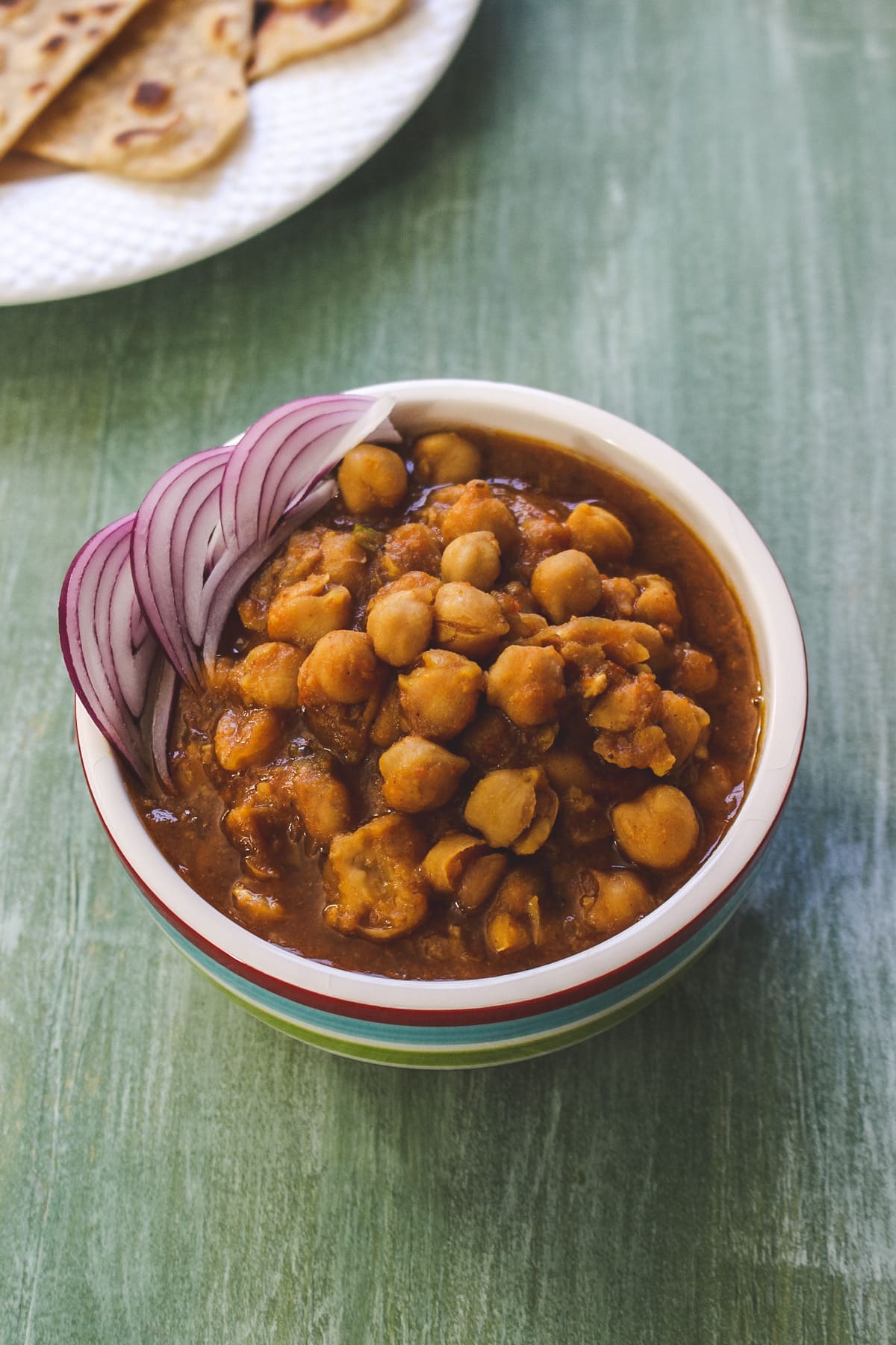 Instant pot chana masala garnished with sliced onions, served with paratha.