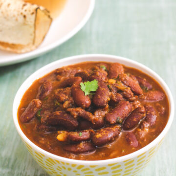 Instant pot rajma in a bowl with cilantro leave, served papad and rice on the side.