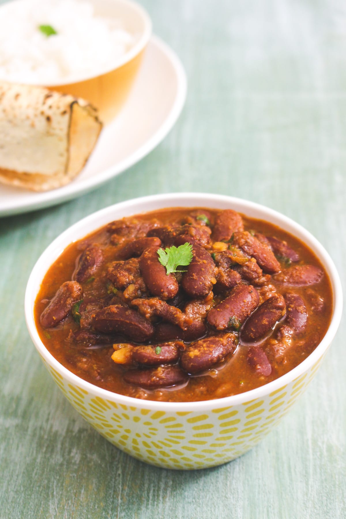 Instant pot rajma in a bowl with cilantro leave, served papad and rice on the side.